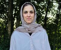 Dr Maria Aslam is looking directly at the camera, she is wearing a light-coloured striped shirt and grey hijab.